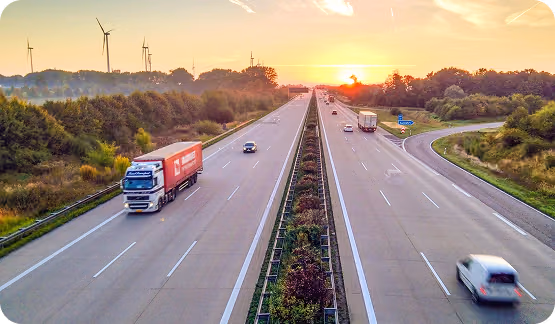 Aerial view of a six lane highway at sunset with a windfarm in the distance